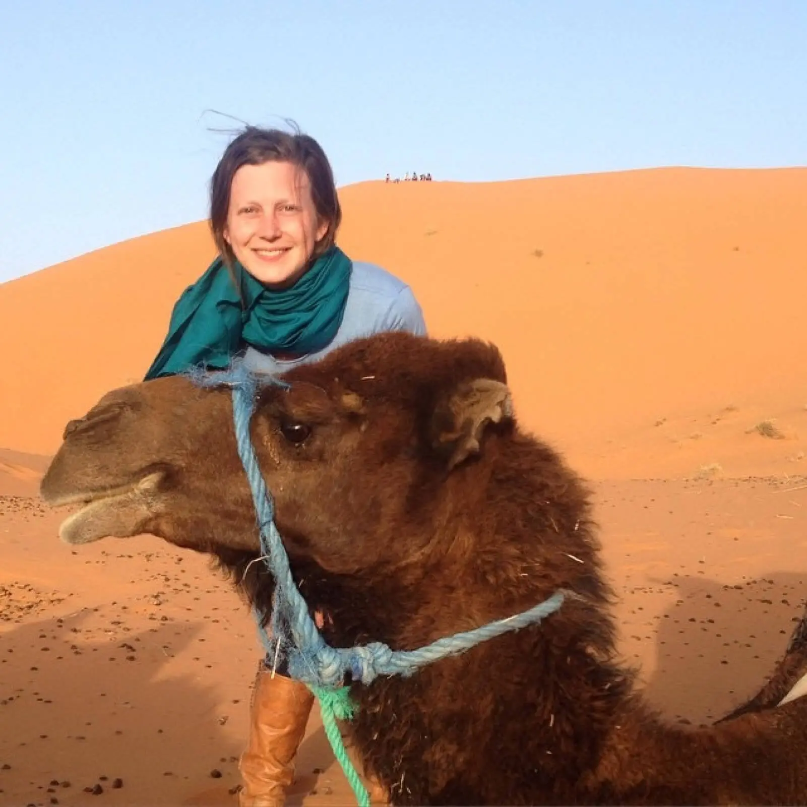 Fabric employee Sarah in Morocco, smiling by sand dunes with a camel.
